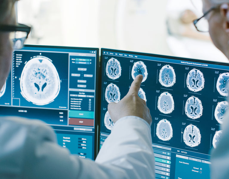 Médico analisando imagens de raio-x de um cérebro que estão sendo exibidas em monitores.